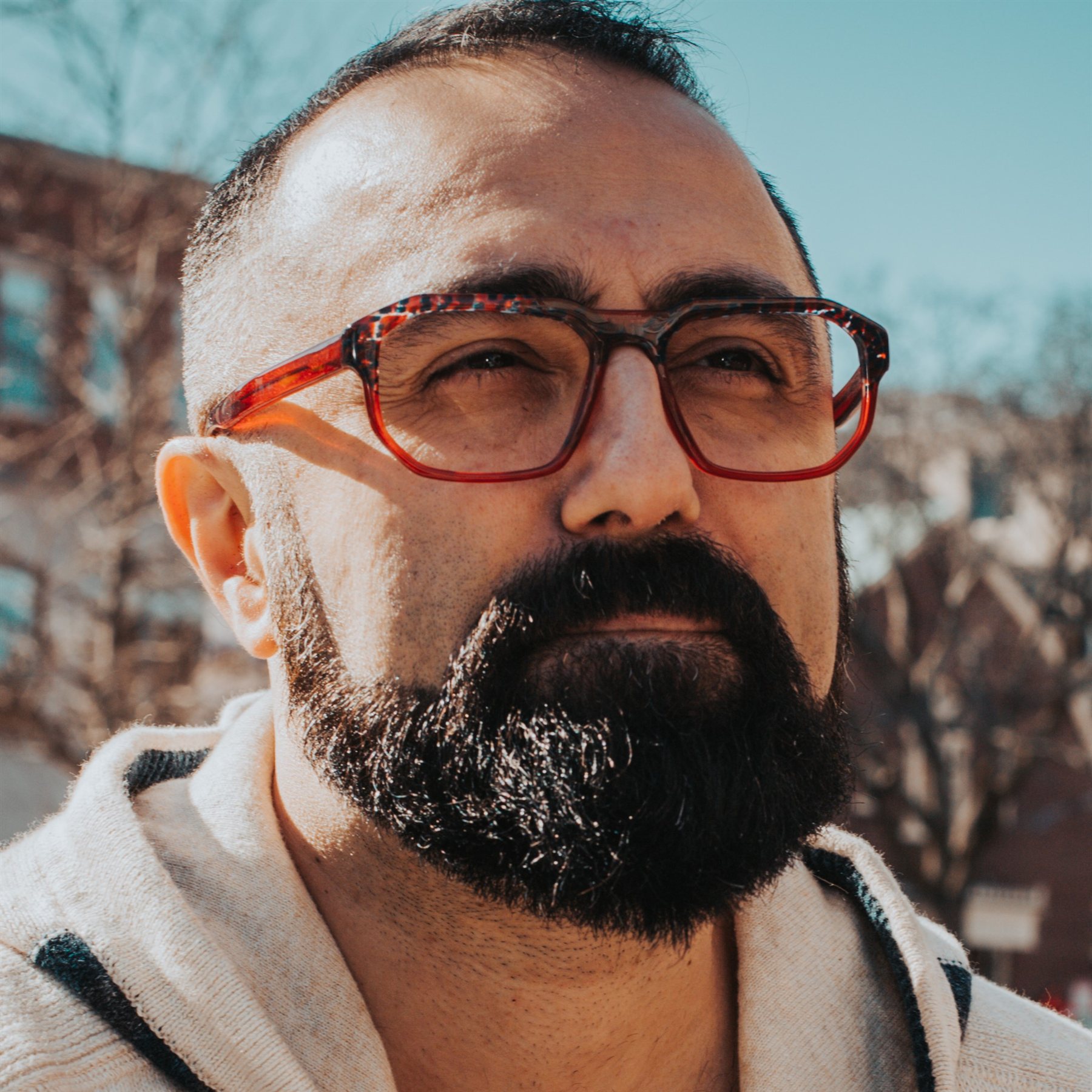 Close-up portrait of Andy outdoors in bright sunlight, wearing red glasses.
