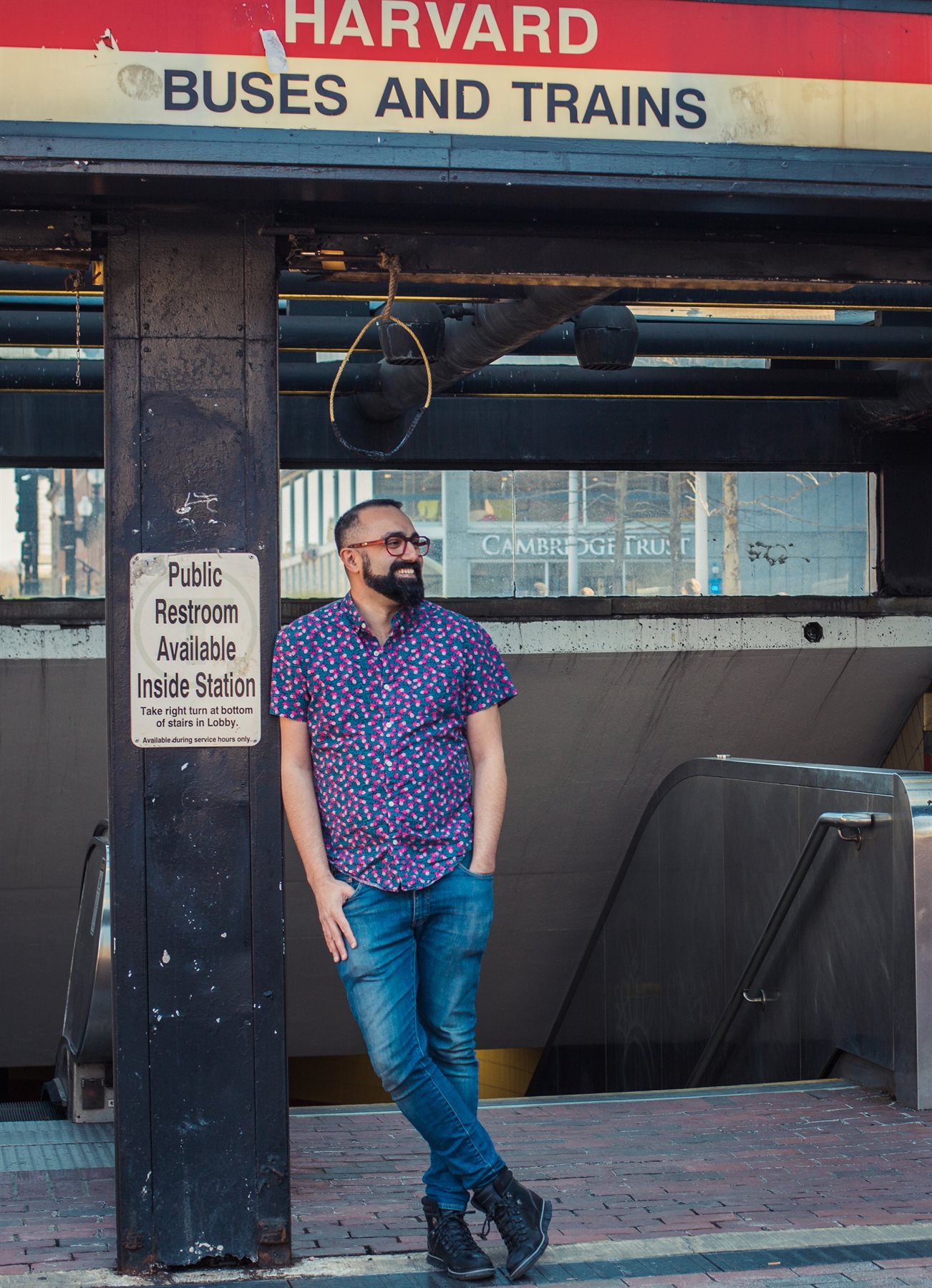 Andy in a blue floral shirt stands below the Harvard Buses and Trains station sign.