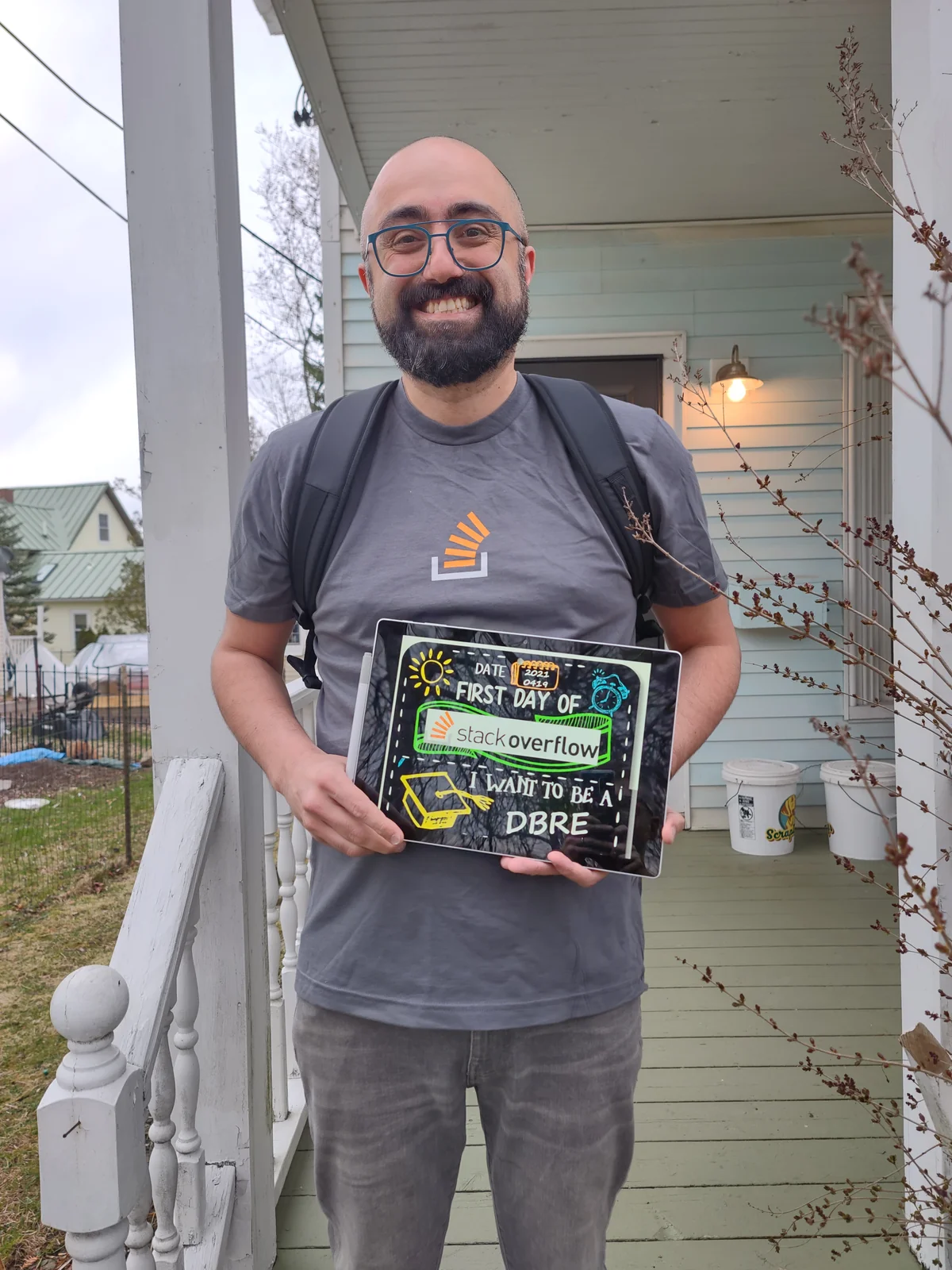 Andy Mallon wearing a Stack Overflow T-shirt and backpack, holding a sign marking his first day as a DBRE on April 19, 2021.