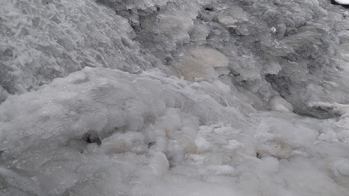 Water moves beside ice forming along the waterfall edges.