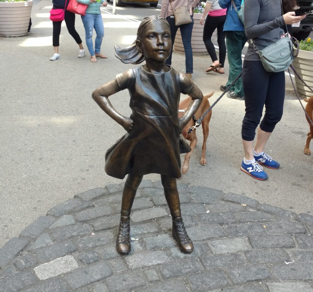 Fearless Girl statue outside the New York Stock Exchange, with a dog behind her.