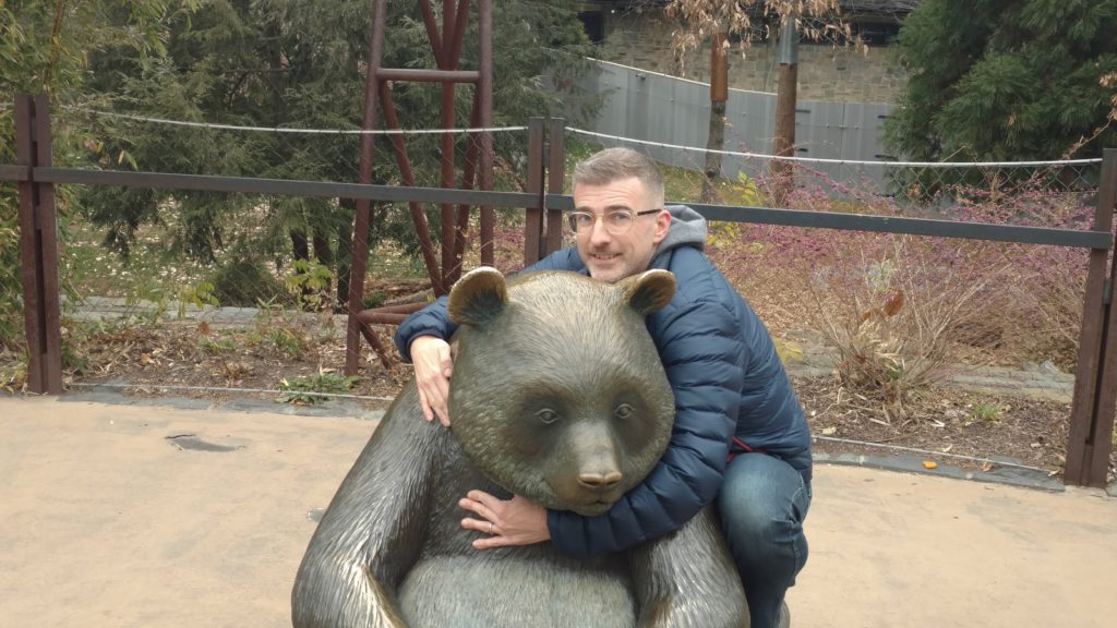 A man stands near a panda at the zoo.