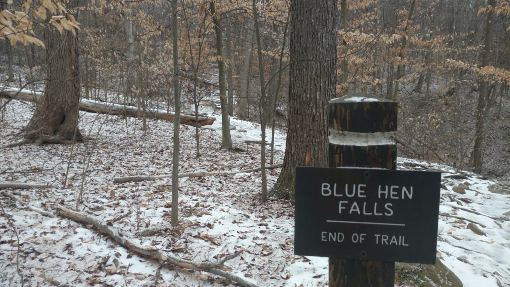 A trail sign marks the end of the trail beside the snowy path.