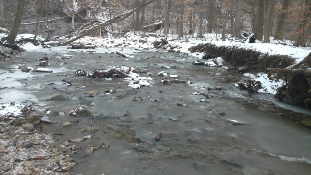 Snow hides the path at a stream crossing.